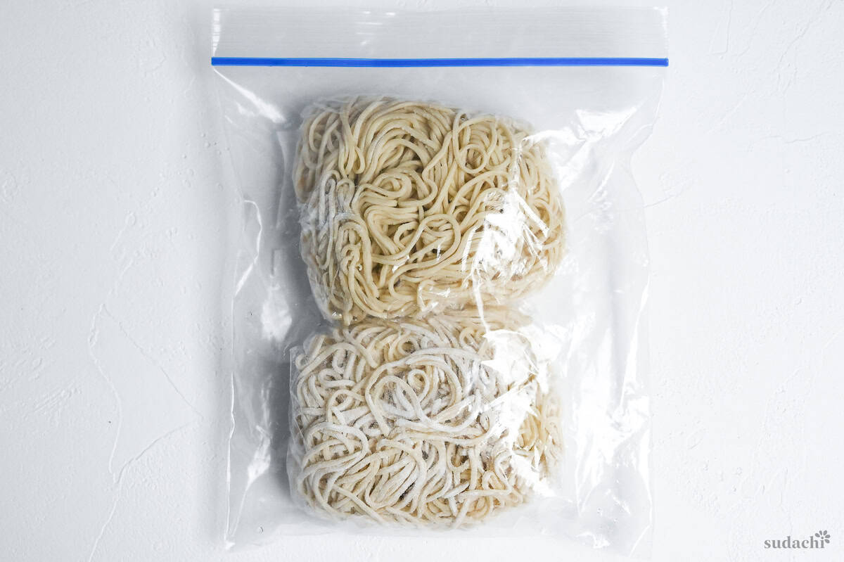 two bundles of ramen noodles wrapped with plastic wrap and stored in a sealed freezer bag