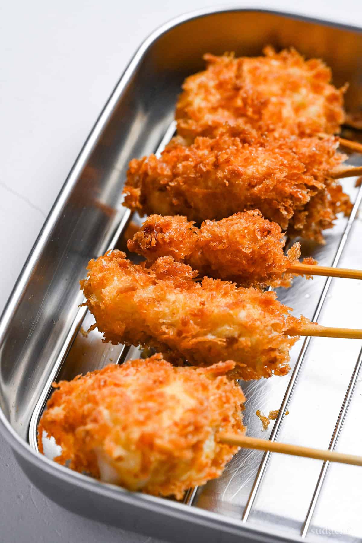 battered kushi age skewers resting on a wire rack after frying