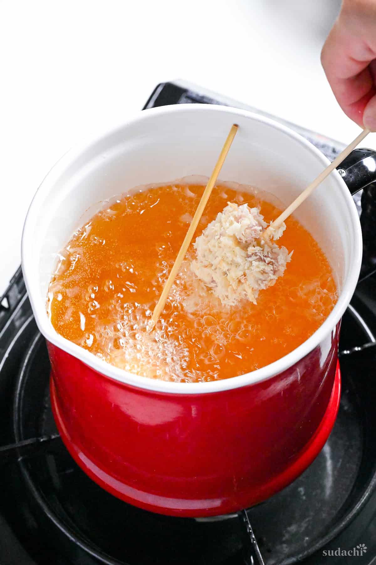 placing kushi age battered skewer into hot oil on the stove