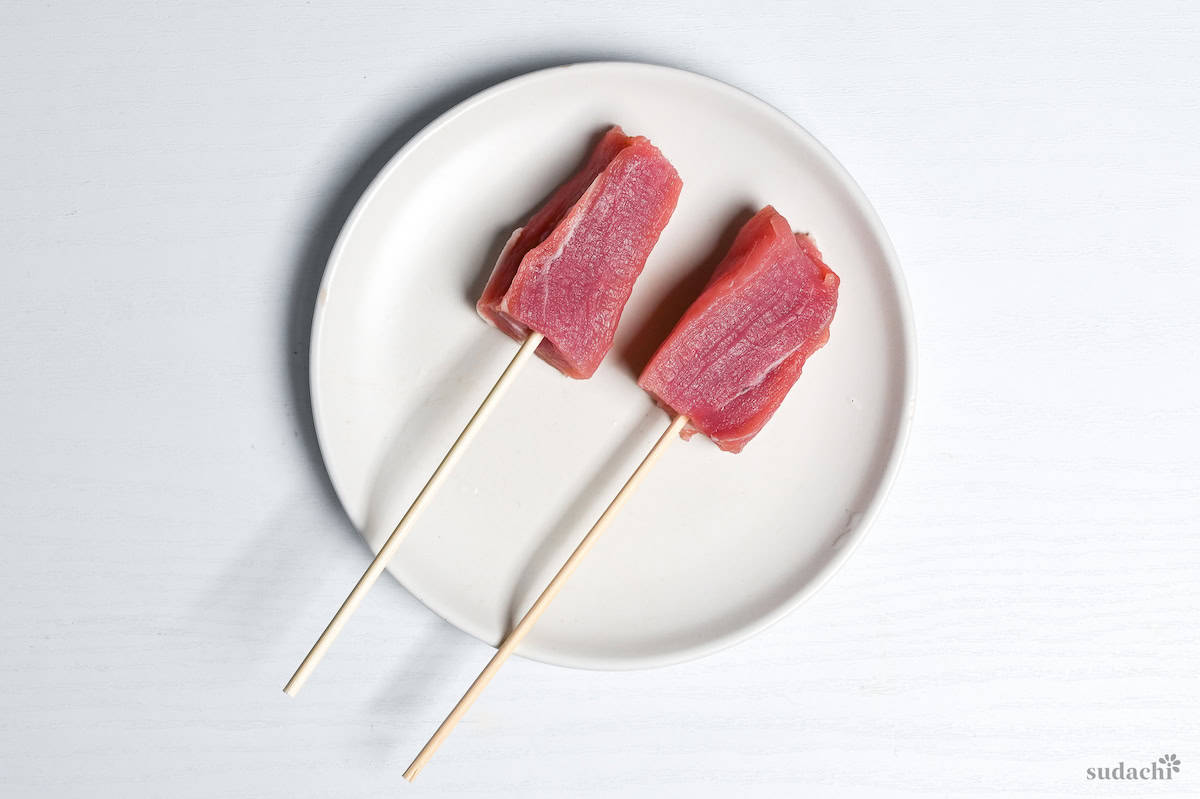 Two pieces of pork on bamboo skewers on a white plate on a white background