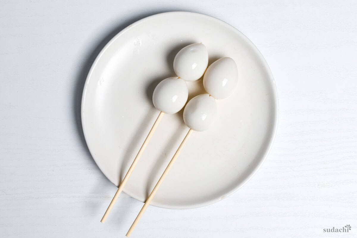 4 boiled quail eggs on bamboo skewers on a white plate on a white background