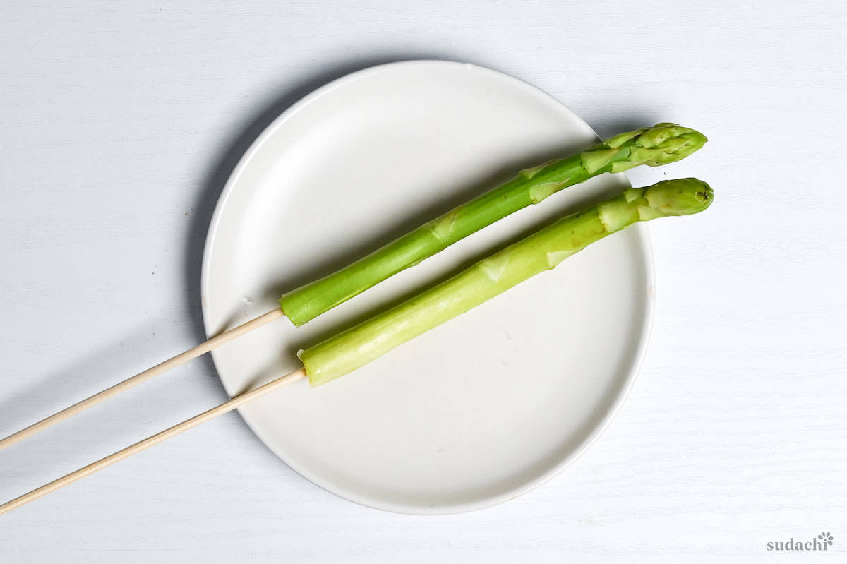 two asparagus stalks on bamboo skewers on a white plate on a white background