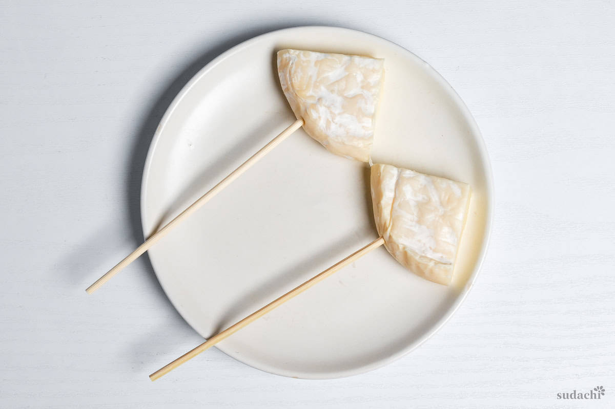 two triangles of Camembert cheese on bamboo skewers on a white plate on a white background