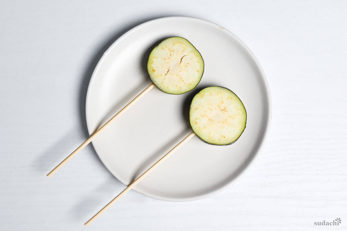 two eggplant rounds on bamboo skewers on a white plate on a white background