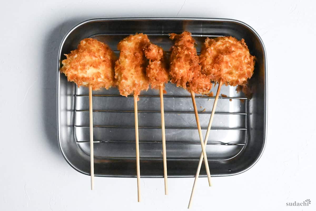 kushi age skewers resting on a wire rack in a steel container