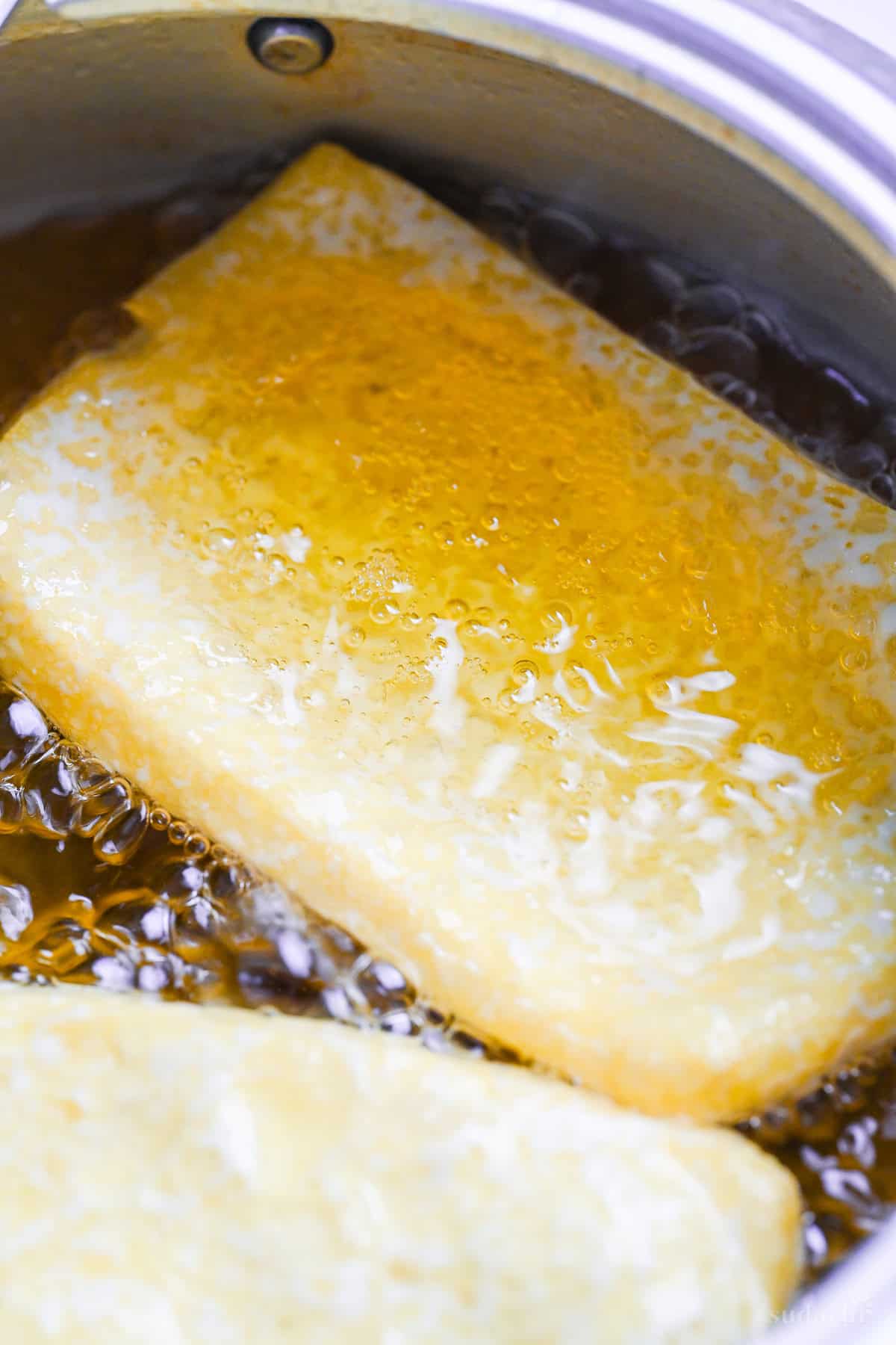 Close up of frying homemade aburaage (twice fried tofu pouches) in a pot of oil