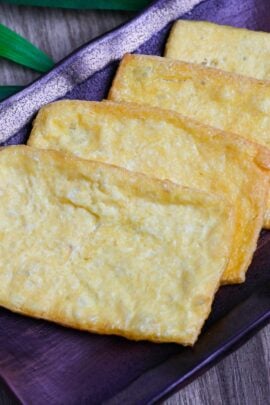 Four slices of homemade aburaage (twice fried tofu pouches) on a deep brownish purple rectangular plate