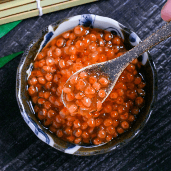 Homemade cured (marinated) salmon roe (ikura) in a small brown bowl and on a brown ceramic spoon
