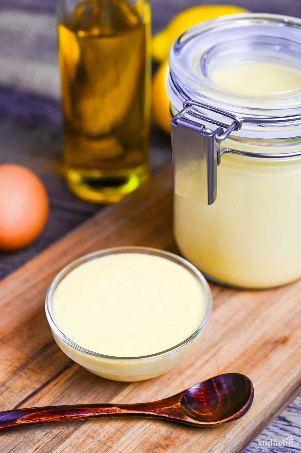 Homemade Kewpie Style Japanese Mayonnaise in a glass jar and glass bowl on a wooden chopping board with ingredients in the background