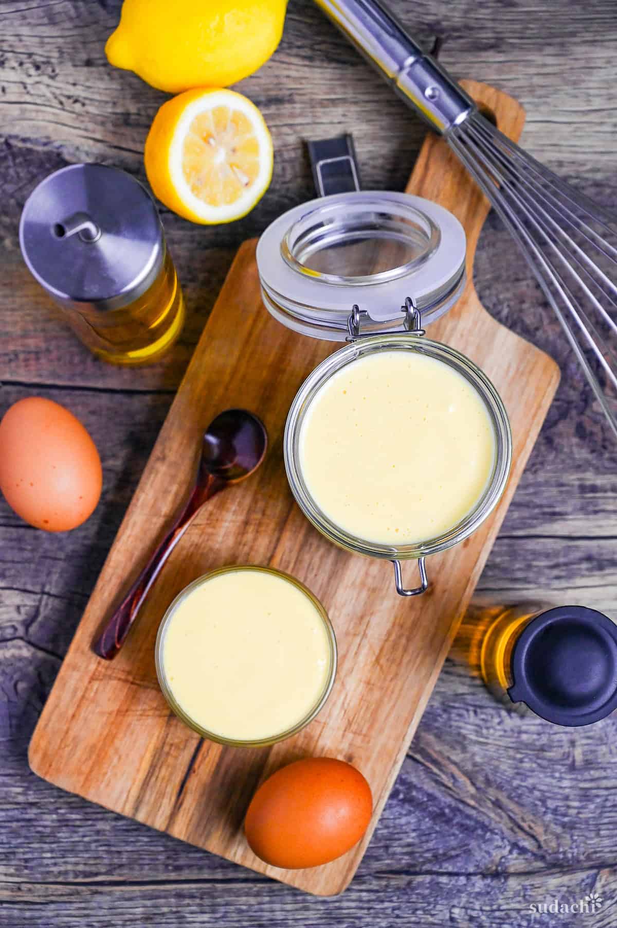 Homemade Japanese Mayonnaise (Kewpie Style) in a glass jar and glass bowl on a wooden chopping board with ingredients scattered around