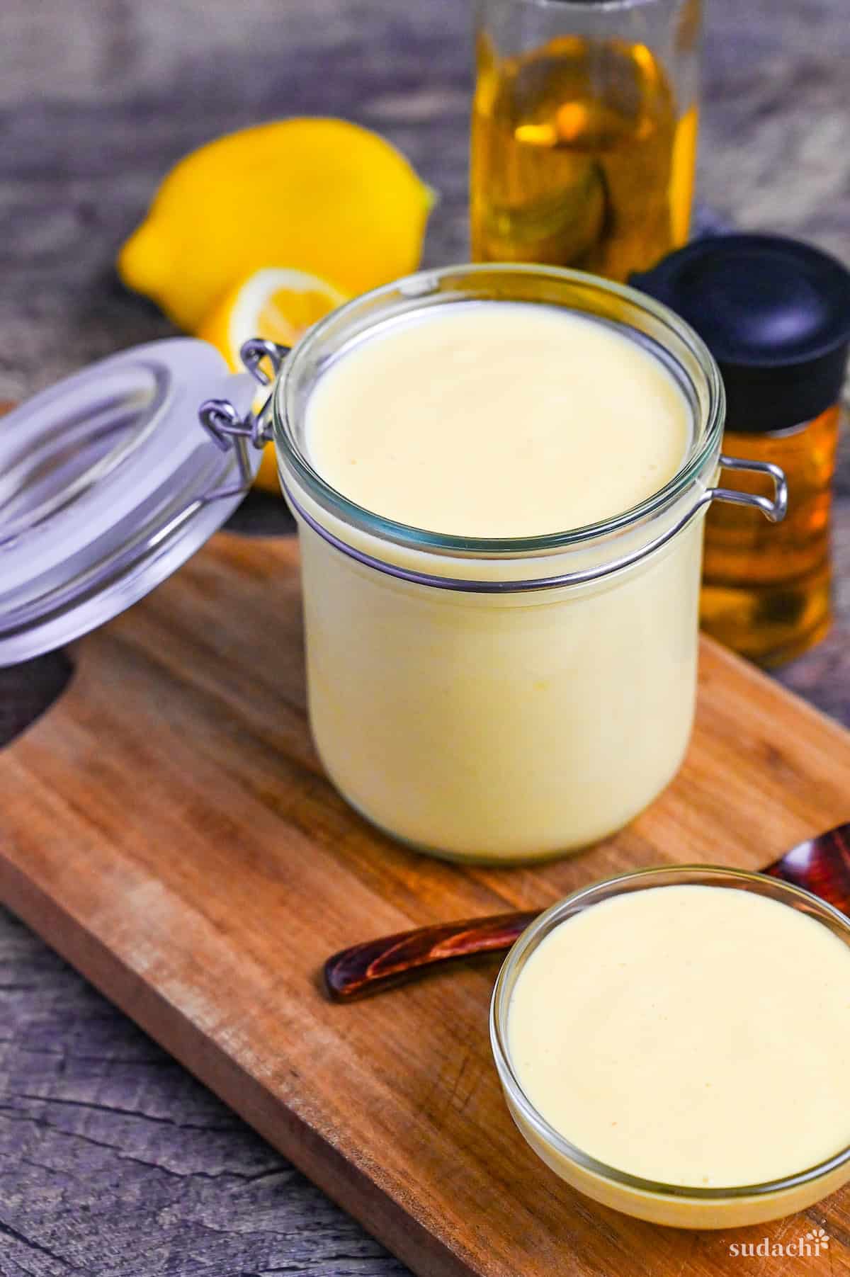 Homemade Japanese Mayonnaise (Kewpie Style) in an open glass jar and glass bowl on a wooden chopping board with ingredients in the background