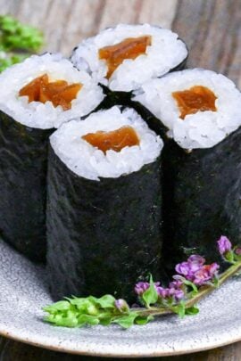 Four pieces of kanpyo maki (simmered gourd sushi rolls) on a white and gray crack-effect plate decorated with real purple flowers