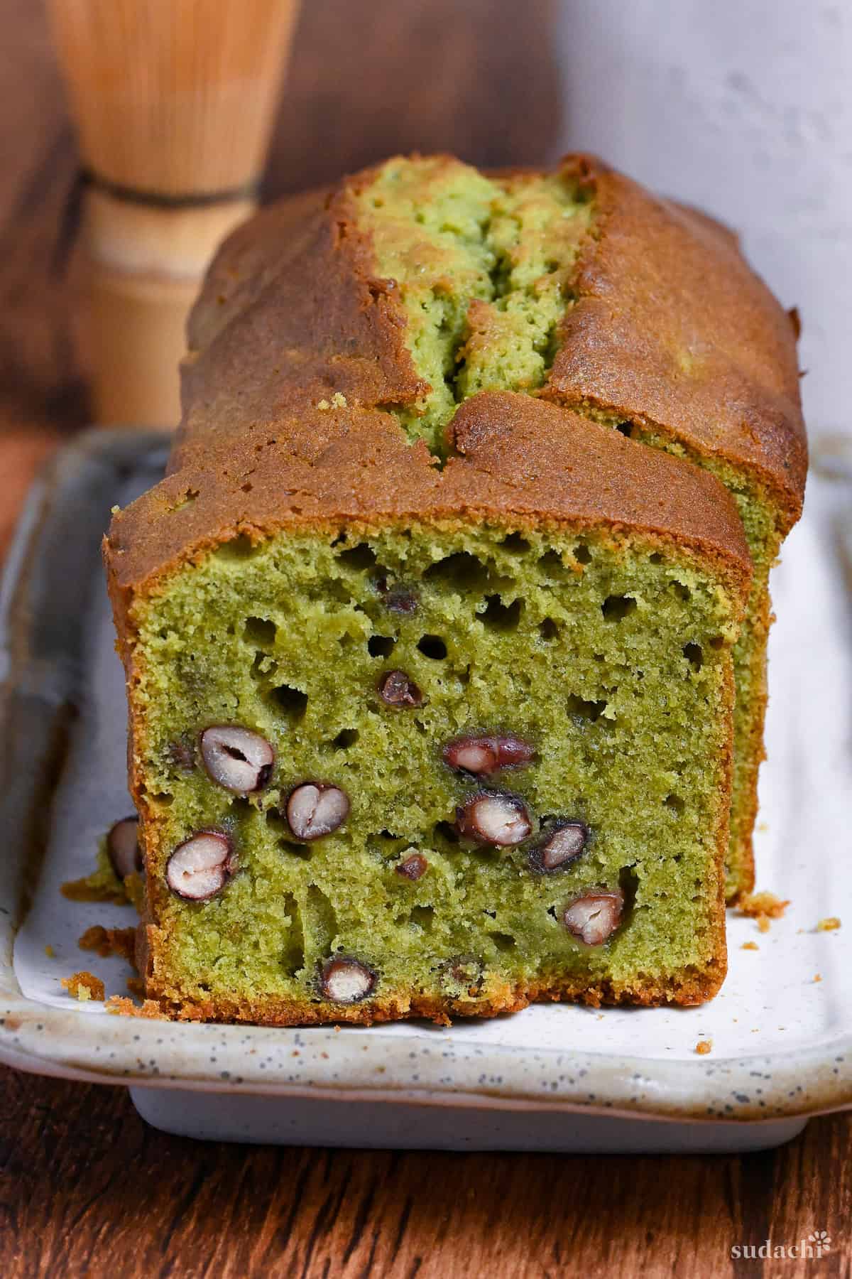 Matcha and adzuki bean poundcake with a slice cut on a cream colored rectangular plate on a wooden surface