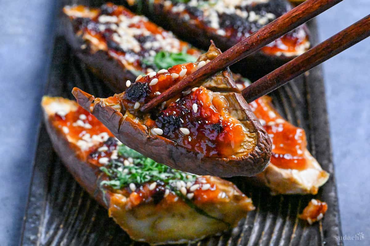 A piece of miso-glazed eggplant (nasu dengaku) held up with wooden chopsticks
