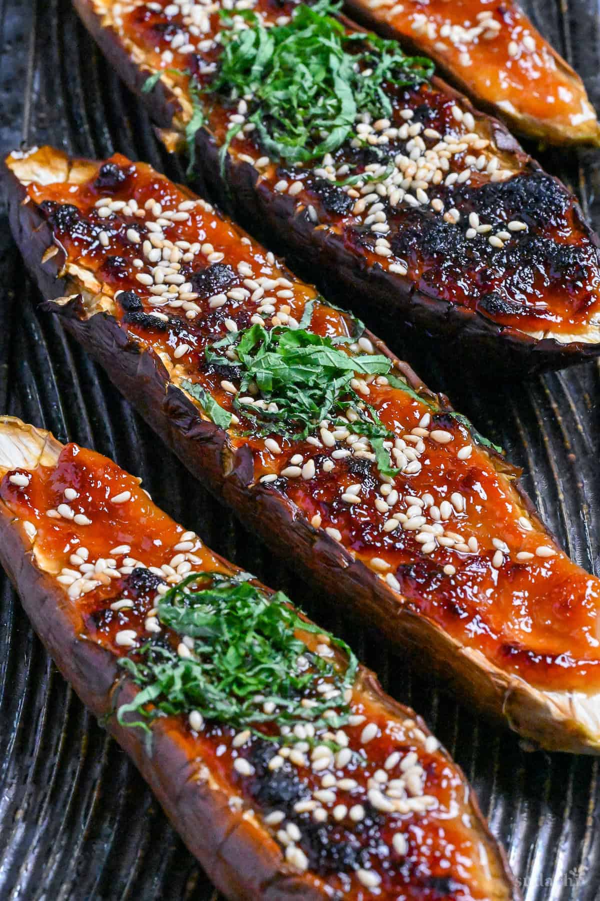 Nasu dengaku (Japanese miso-glazed eggplant) sprinkled with sesame seeds and shredded Perilla leaves on a dark textured rectangular plate