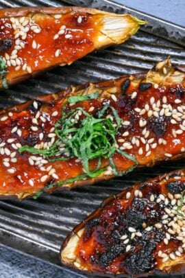 Nasu dengaku (Japanese miso-glazed eggplant) sprinkled with sesame seeds and shredded Perilla leaves on a dark textured rectangular plate