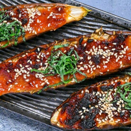 Nasu dengaku (Japanese miso-glazed eggplant) sprinkled with sesame seeds and shredded Perilla leaves on a dark textured rectangular plate