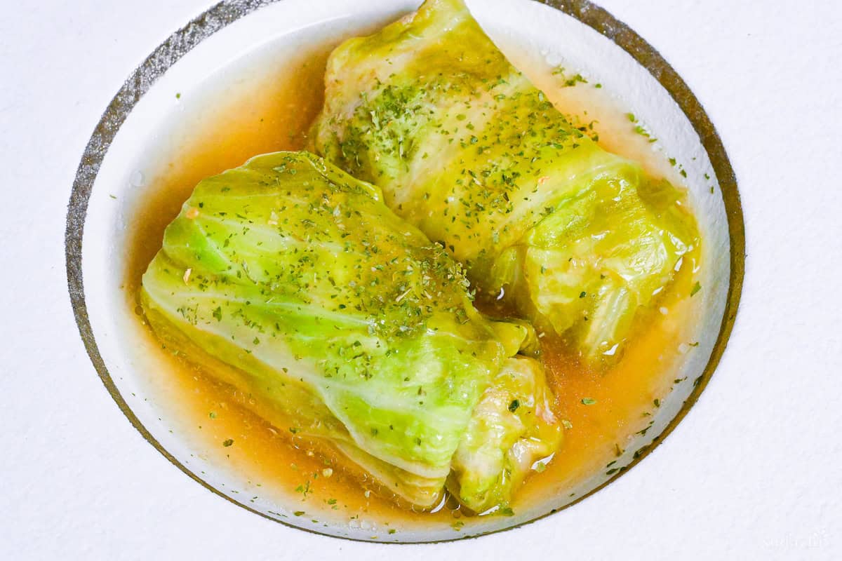 Two Japanese cabbage rolls (Roll Kyabetsu) on a white plate in a homemade sauce and sprinkled with parsley