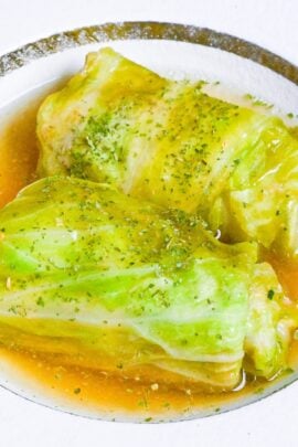 close up of two Japanese cabbage rolls (Roll Kyabetsu) on a white plate in a homemade sauce and sprinkled with parsley