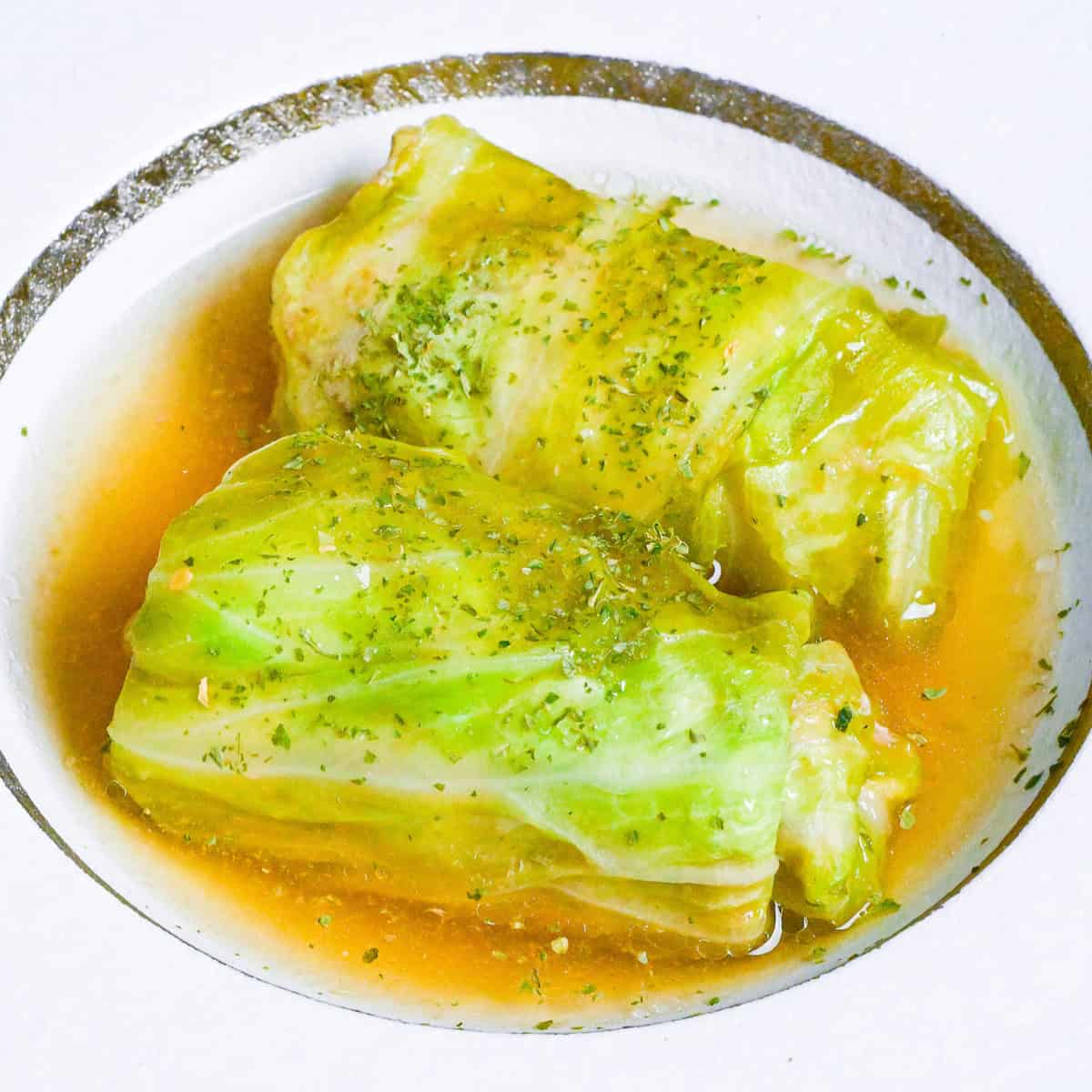 close up of two Japanese cabbage rolls (Roll Kyabetsu) on a white plate in a homemade sauce and sprinkled with parsley