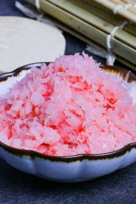 Homemade sakura denbu (fluffy pink fish flakes) made with cod in a white fluted bowl with brown rim on a gray background