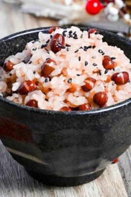 sekihan (red bean rice) in a black rice bowl sprinkled with coarse salt and black sesame seeds on a light wooden surface