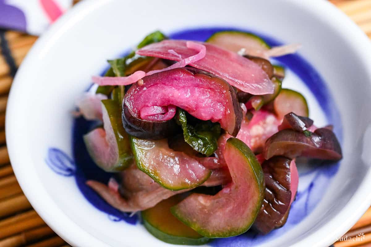 Homemade purple shibazuke pickles made with eggplant, cuucmber, Japanese ginger and ginger in a white dish with eel design close up