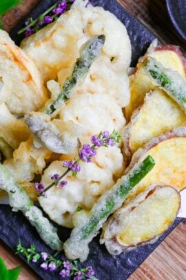 Eggless Vegetable Tempura (shojin-age) with homemade matcha salt served on a square black plate decorated with purple flowers