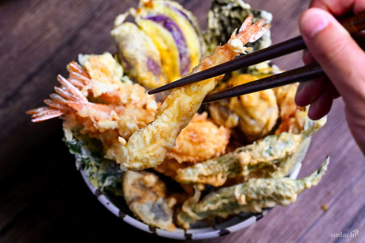holding one tempura shrimp with chopsticks over a tempura rice bowl