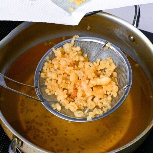 scooping crispy tenkasu tempura flakes out of hot oil using a mesh spoon