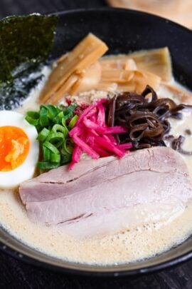 easy shortcut tonkotsu-style ramen topped with pork chashu, ramen egg and shredded vegetables in a black bowl on black wood-effect background