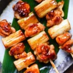 three negima yakitori Japanese chicken skewers on an oval plate with decorative leaf