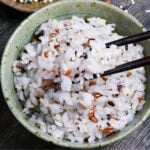 Japanese multigrain rice (zakkokumai) in a green and brown ceramic rice bowl surrounded by various grains and seeds