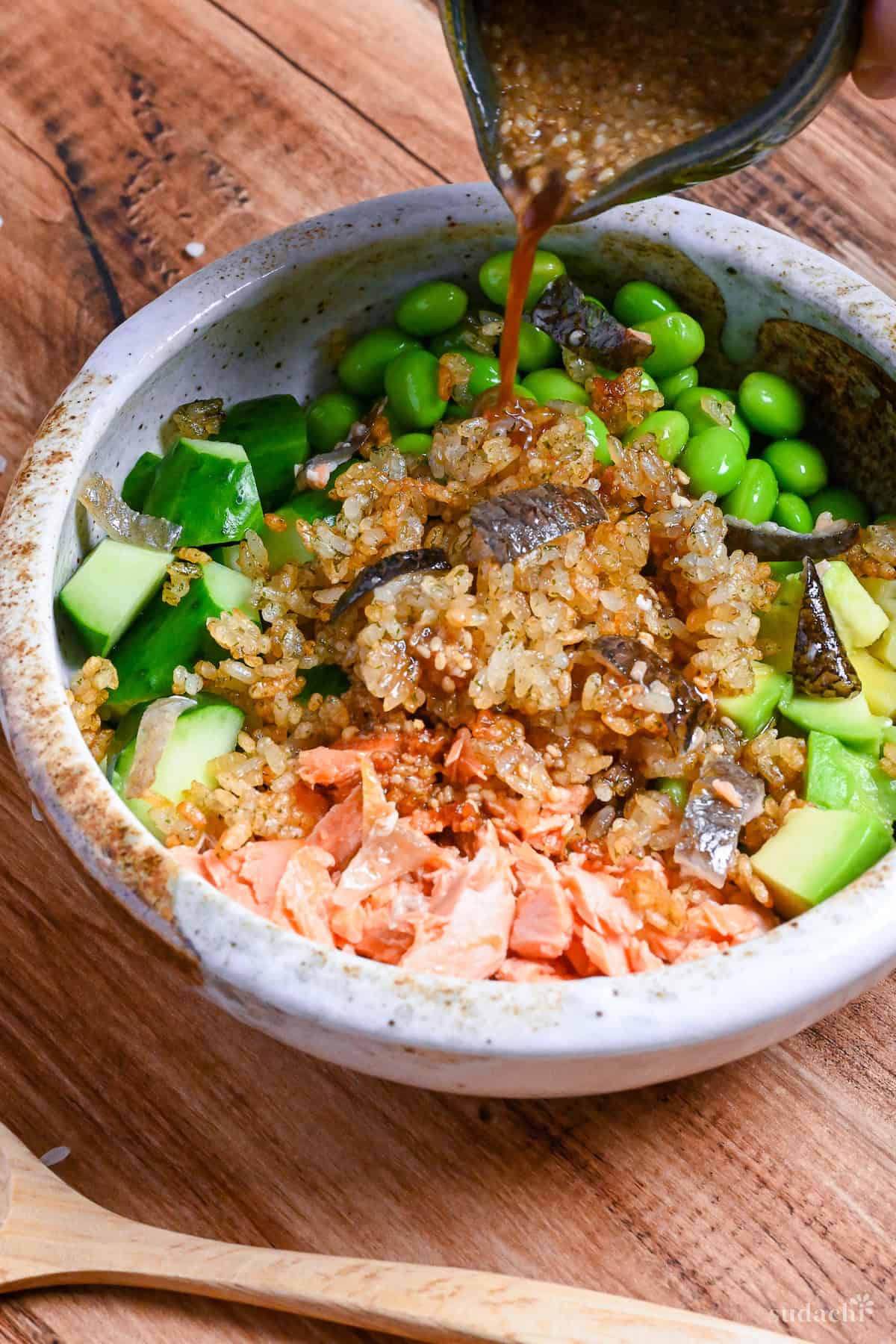 pouring yuzu dressing over Japanese style crispy rice salad in a mottled cream and brown bowl