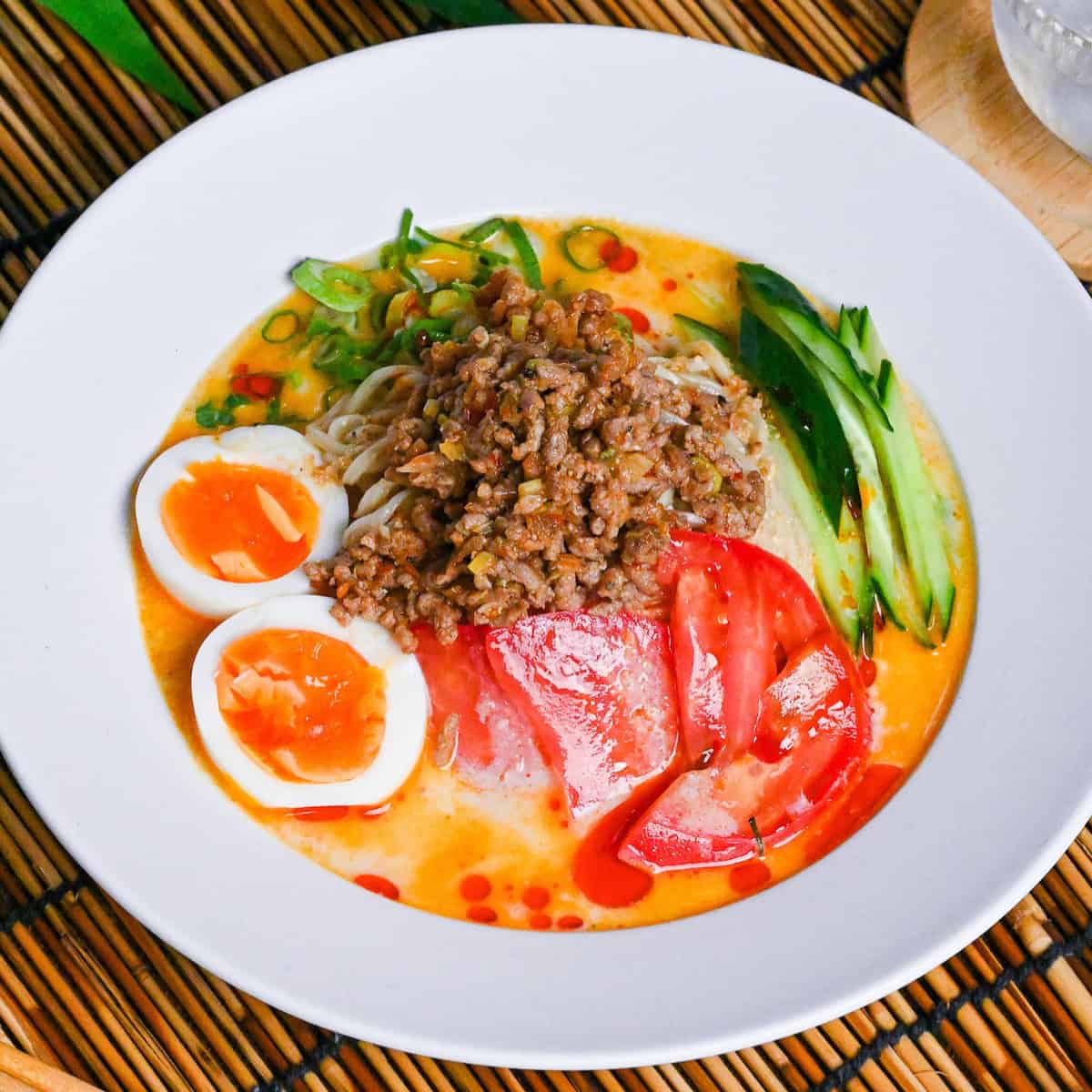 Cold (hiyashi) tan tan ramen in a white bowl topped with ground pork, soft boiled eggs and vegetable