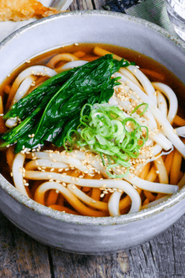 Koro udon topped with blanched spinach, chopped green onions and sesame seeds in a gray ceramic bowl