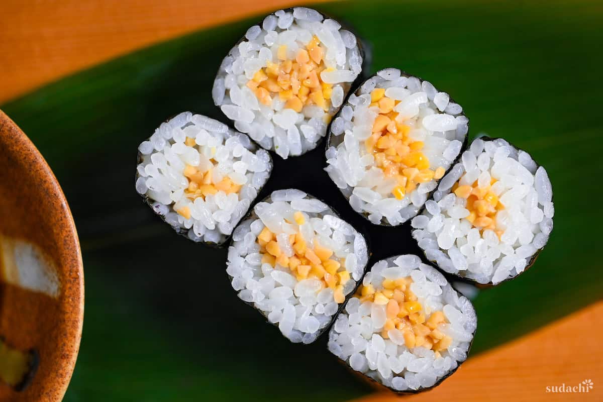 Six pieces of natto maki (fermented soybeans sushi rolls) on a green leaf on a wooden platform