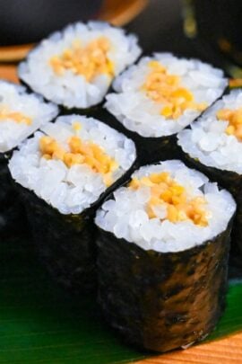 Six pieces of natto maki (fermented soybeans sushi rolls) on a green leaf on a wooden platform