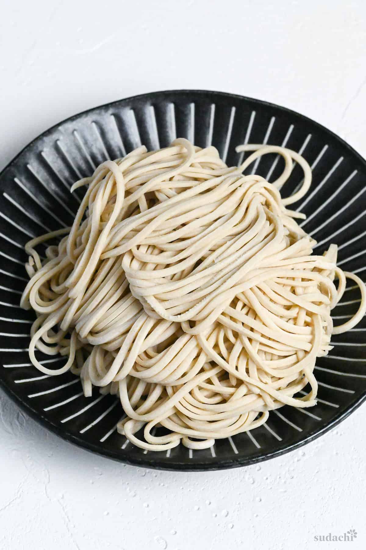 Homemade ramen noodles (uncooked) with lower water percentage on a black plate with white stripes on a white mottled background