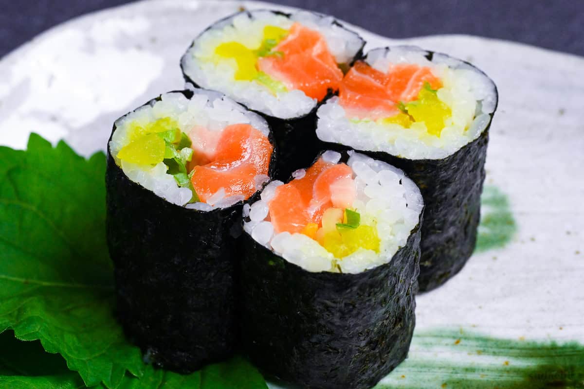 Four pieces of salmon sushi rolls with finely chopped daikon pickles and green onions on a gray plate with green brushstroke design