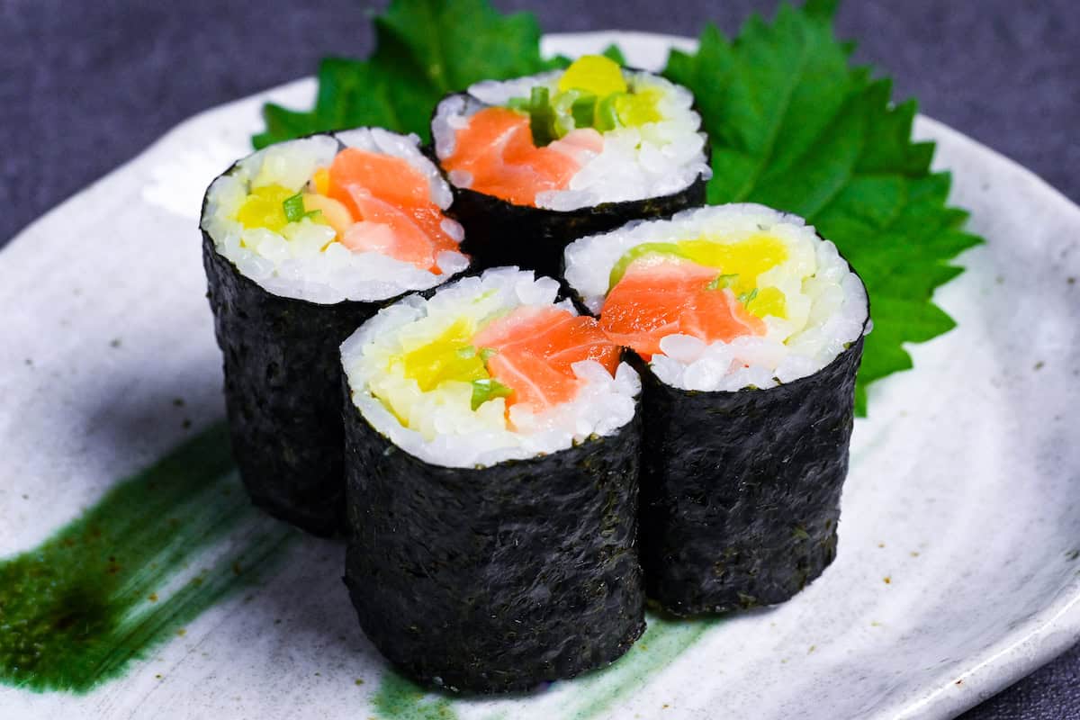 Four pieces of salmon sushi rolls with finely chopped daikon pickles and green onions on a gray plate with green brushstroke design
