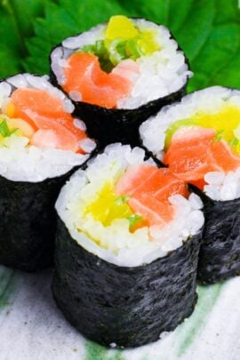 Four pieces of salmon sushi rolls with finely chopped daikon pickles and green onions on a gray plate with green brushstroke design