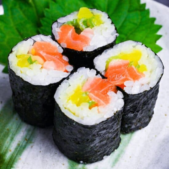 Four pieces of salmon sushi rolls with finely chopped daikon pickles and green onions on a gray plate with green brushstroke design