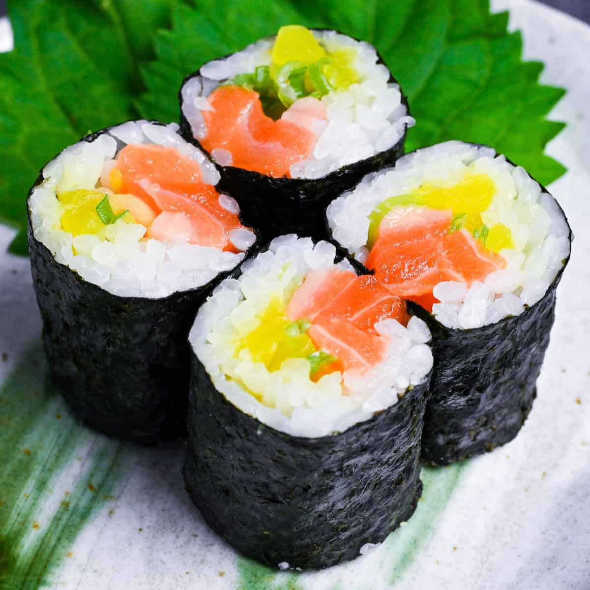 4 salmon and pickles sushi rolls on a gray plate with green brush design