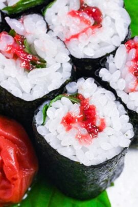 Six pieces of ume shiso maki (pickled plum & perilla leaf sushi rolls) on a cream speckled plate close up