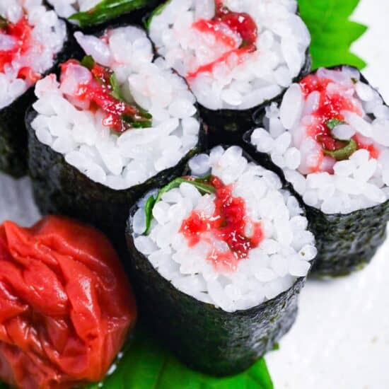 Six pieces of ume shiso maki (pickled plum & perilla leaf sushi rolls) on a cream speckled plate close up