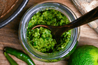 Homemade yuzu kosho made with unripe green yuzu and green chilis in a glass jar on a wooden chopping board