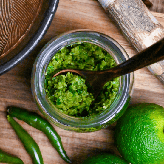 Homemade yuzu kosho made with unripe green yuzu and green chilis in a glass jar on a wooden chopping board