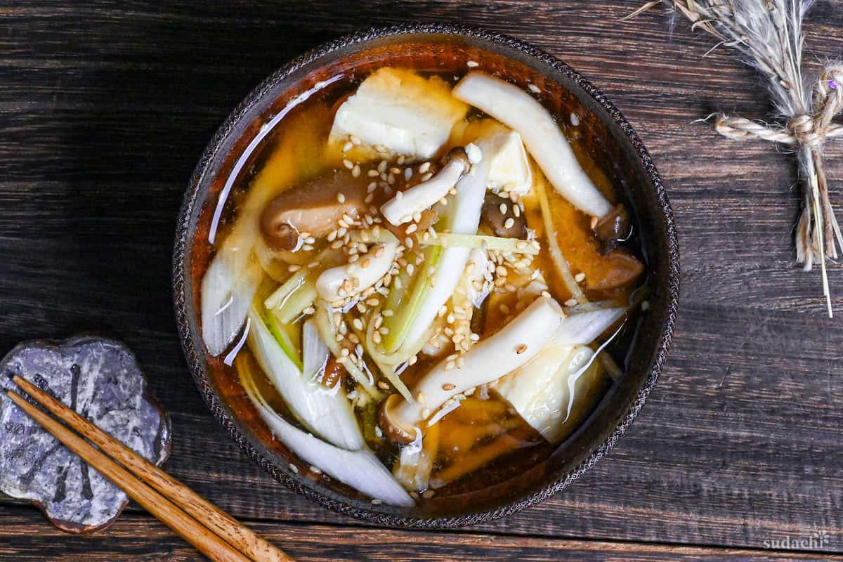 Ginger infused plant-based miso soup sprinkled with sesame seeds in a wooden bowl with brown rim