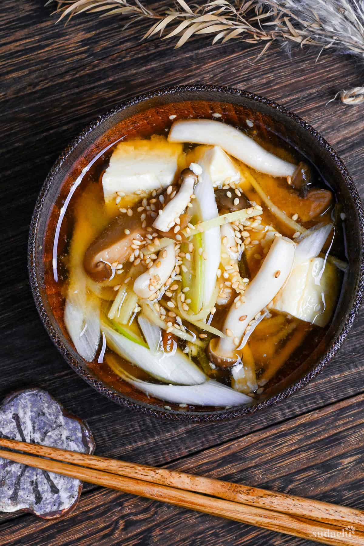 Ginger infused plant-based miso soup sprinkled with sesame seeds in a wooden bowl with brown rim